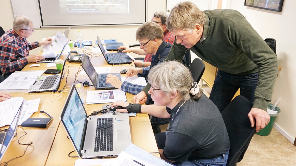 Fyra peroner sitter framför varsin dator i ett mötesrum. Närmast kameran sitter en medelålders kvinna och arbetar med digitala skogsbruksplanen i datorn. Bakom/bredvid henne står en medelålders man lutad över henne. Båda tittar in i datorskärmen.