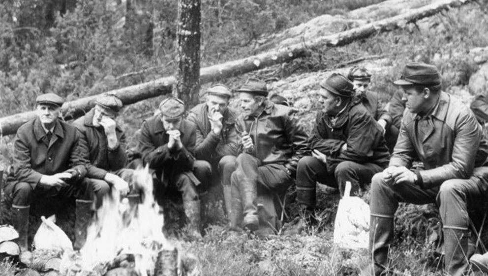 Män som sitter i skog vid en eld.