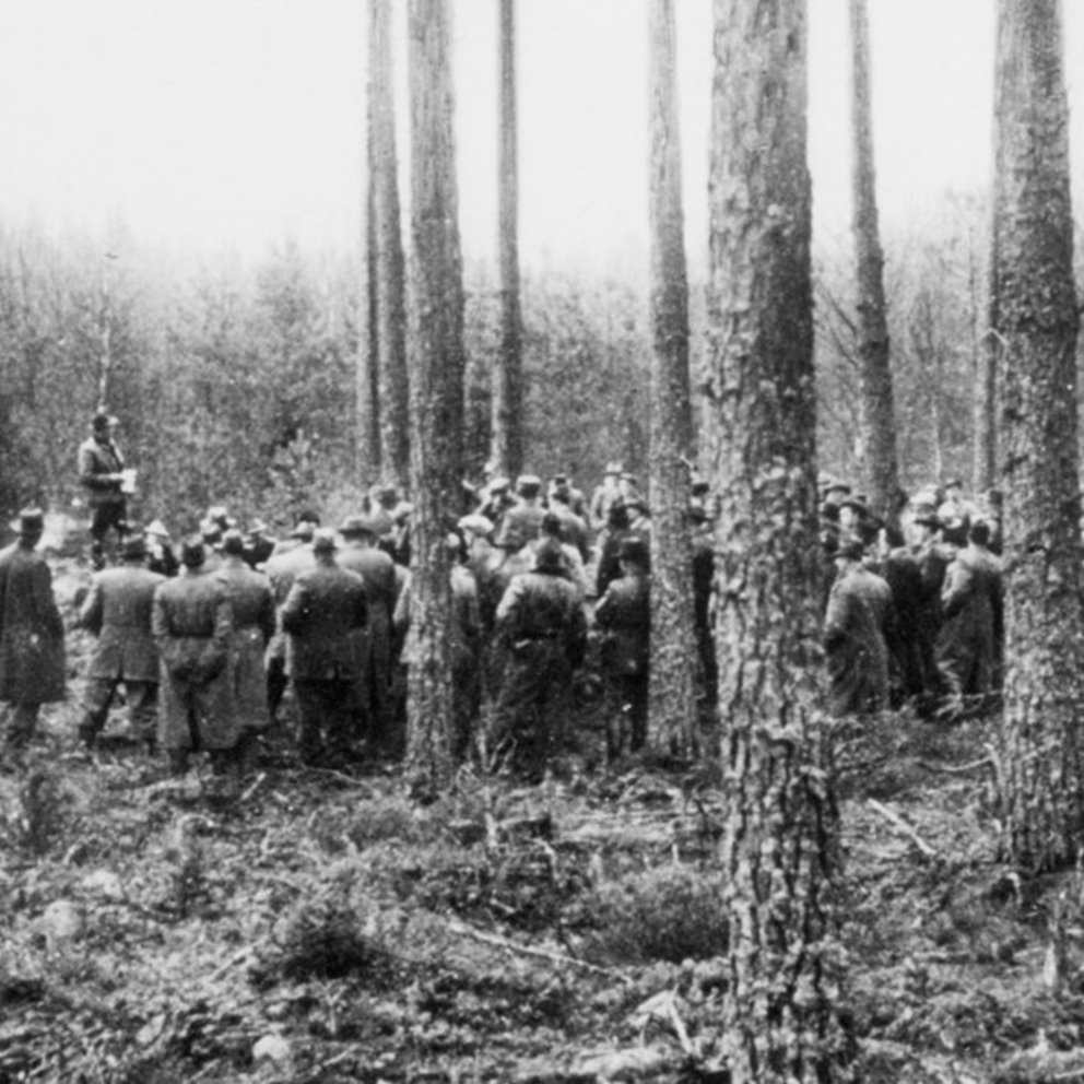 Svart vit bild med människor samlade i skogen som diskuterar