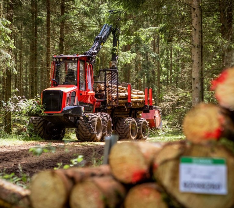 Skogsmaskin bakom en virkes hög med virke från en medlem i Södra