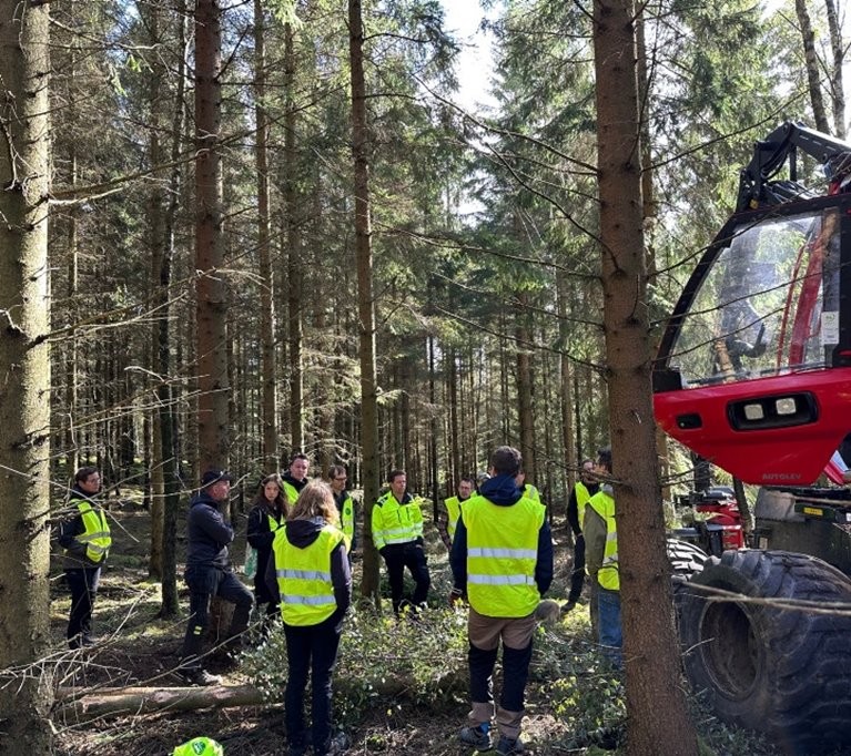 Individer med reflexväst i skog med skogsmaskin