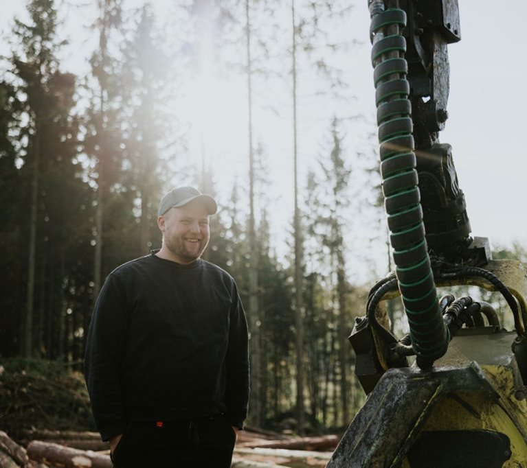 Ung man stående intill skogsmaskin i skogen