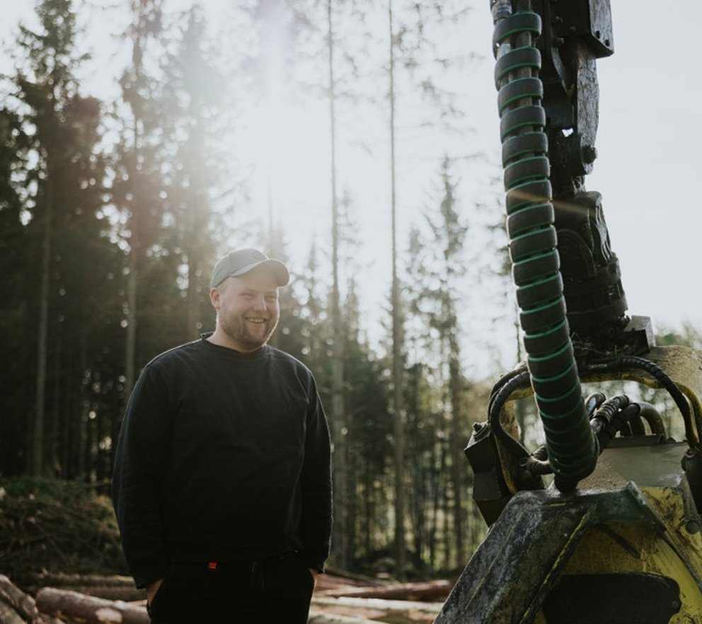 Ung man stående intill skogsmaskin i skogen