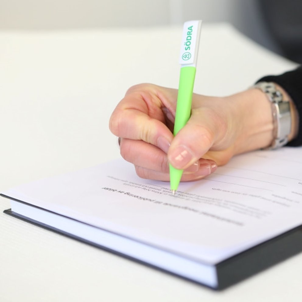 Hand som signerar ett dokument med en grön penna med Södras logotyp.