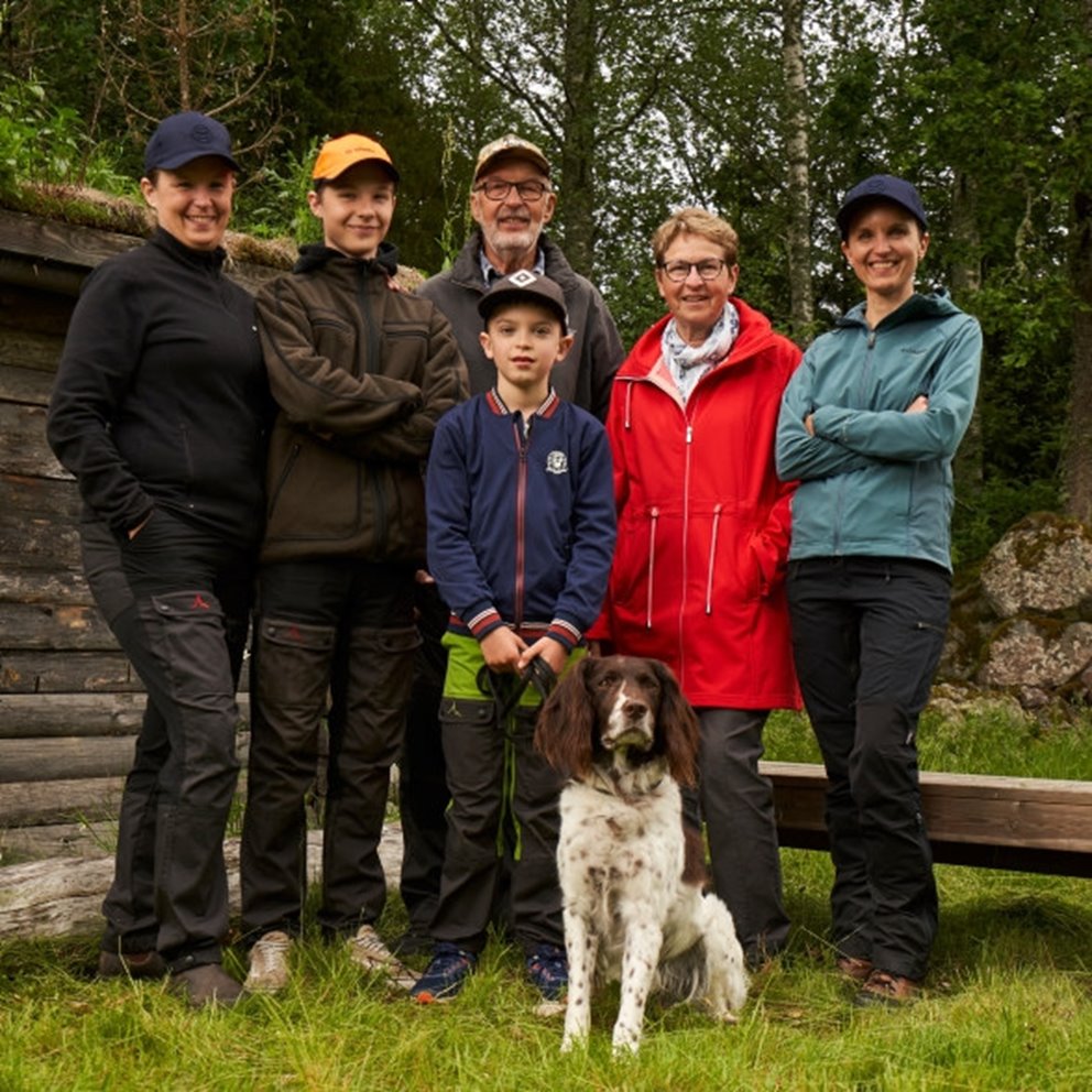 Skogsbrukar familj med hund står utomhus i skogen framför vindskjul