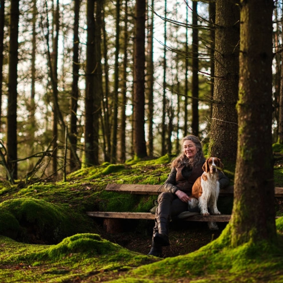 Kvinnlig skogsägare sittandes på bänk med hund