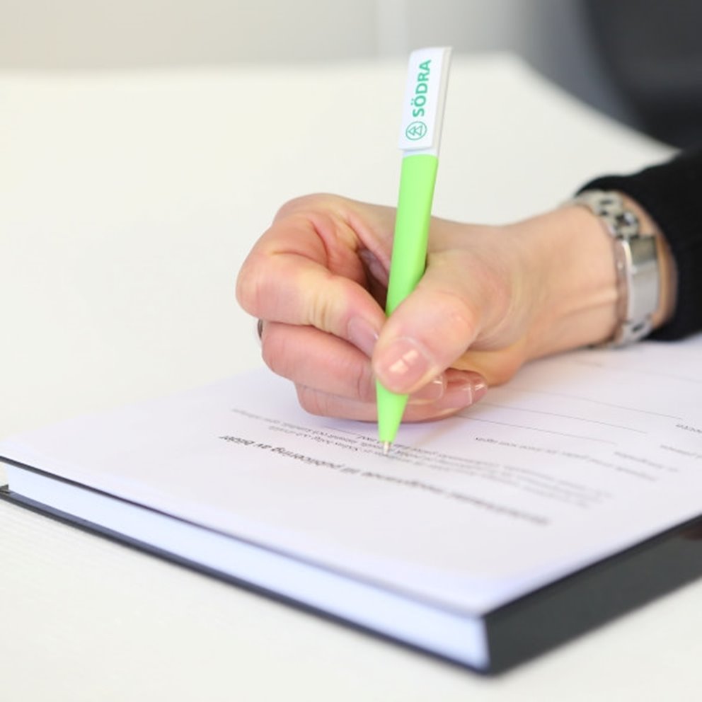 Hand som signerar ett dokument med en grön penna med Södras logotyp.