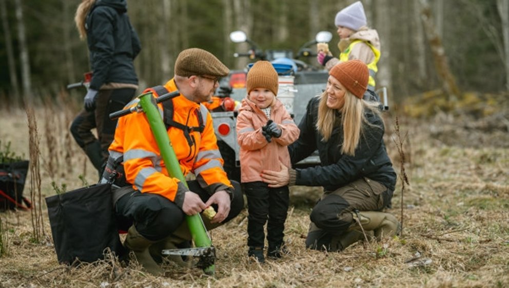 Bild på två föräldrar med ett barn mellan sig tar en paus från plantering av Södras plantor